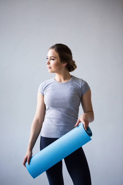 Attractive beautiful young sportswoman holding yoga mat isolated over grey background. - Foto, imagen