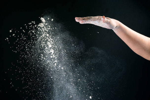 Izolované na černém pozadí ženské ruky nalévá bílou mouku jako sníh na pečení 2020 - Fotografie, Obrázek