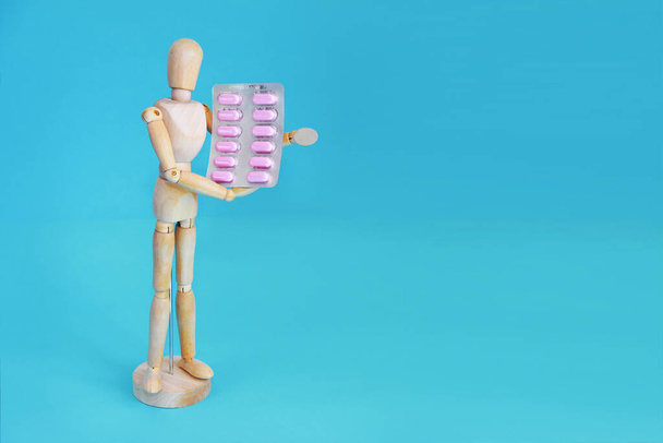 dřevěná žlutá figurína drží růžové lékařské pilulky - Fotografie, Obrázek