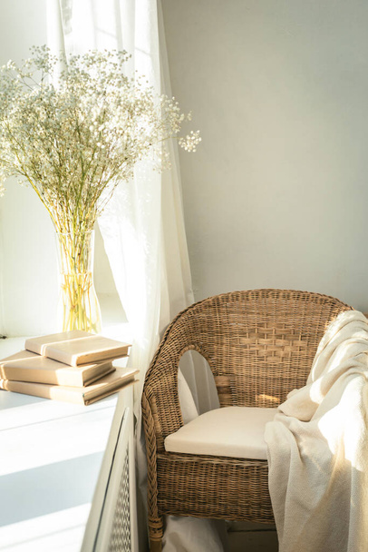 Cozy reading nook by the window with rattan wicker chair, delicate white gypsophila flowers, opened book and window light and shadows.Modern comfortable living room space - Fotó, kép