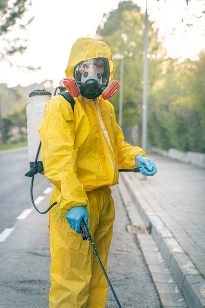 Coronavirus. A sanitation worker wearing a mask and cleaning the streets. Sterilize urban decontaminate city. Disinfecting against to the Coronavirus. Suit protection.  - Fotoğraf, Görsel