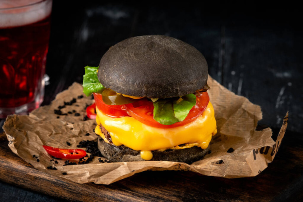 Cheeseburger with a black bun on a kraft paper on wooden Board, homemade Japanese Burger - Photo, image