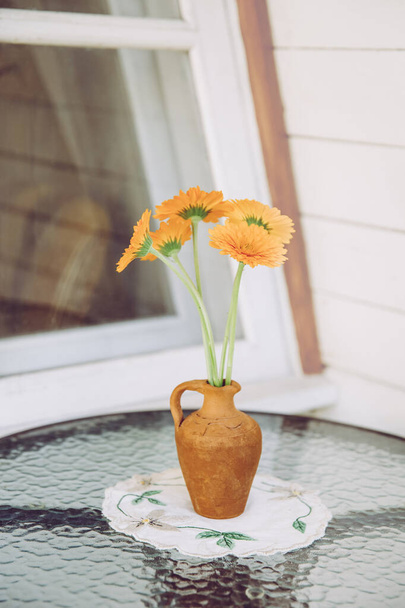 Коричневая глиняная ваза с обычными цветами Мэриголд на столе в саду на балконе
. - Фото, изображение