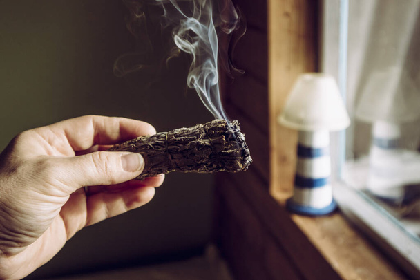 Vrouw hand met kruid bundel gedroogde salie vlek stok roken. Er wordt aangenomen dat negatieve energie te reinigen en te zuiveren woonruimtes thuis in kamers. - Foto, afbeelding