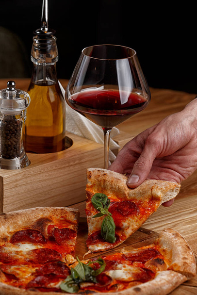 pepperoni pizza és egy pohár bor egy fa asztalon - Fotó, kép