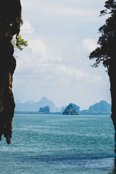 Authentiek uitzicht op het landschap met kopieerruimte van grote zwarte cliff silhouetten op de voorgrond en in de bergen, blauwe golf zeewater en blauw weer warmte op de achtergrond tijdens warme en bewolkte dag in Thailand - Foto, afbeelding