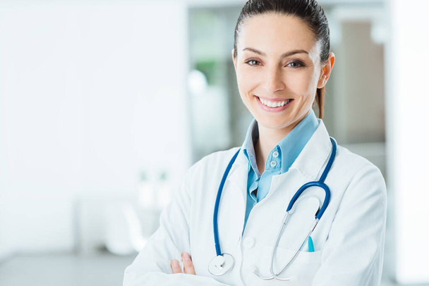 Confident female doctor posing in her office and smiling at camera, health care and prevention concept - Photo, Image