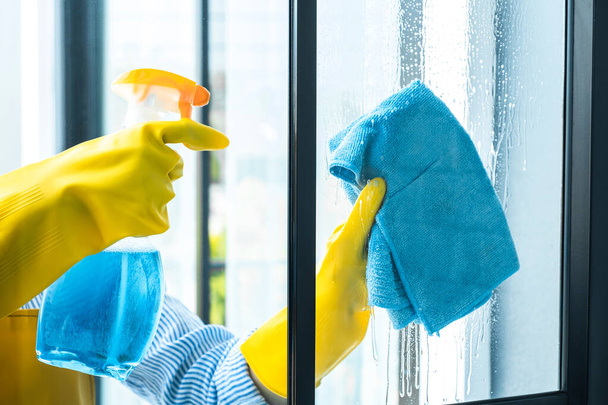 Vaimon siivous- ja siivouskonsepti, onnellinen nuori nainen pyyhkimällä pölyä suihkeella ja pölynimurilla, kun puhdistat lasia kotona
. - Valokuva, kuva