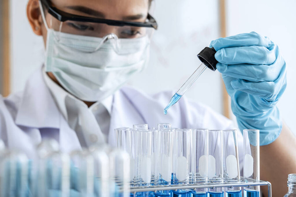 Badania laboratoryjne biochemii, Chemik analizuje próbki w laboratorium ze sprzętem i eksperymentami naukowymi szklanymi zawierającymi płyn chemiczny. - Zdjęcie, obraz