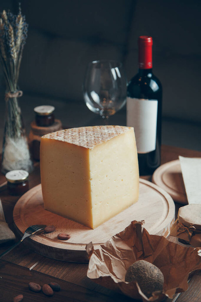 Composition with cheese and wine on a dark background. Slices of cheese and a glass of wine. Large round hard Parmesan cheese.  - Photo, image