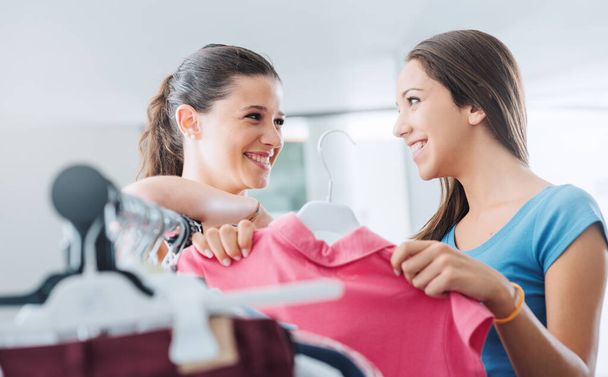 Šťastné usměvavé dospívající dívky nakupování v obchodě a baví, jeden drží růžovou košili - Fotografie, Obrázek