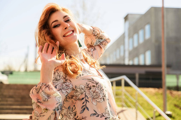Portrait of a happy stylish beautiful woman with long hair on the background of the steps of the building in spring in the sun in bright weather. - Fotografie, Obrázek