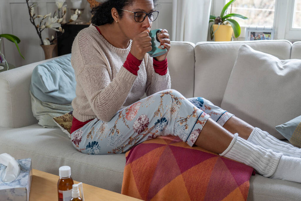 Mujer tomando té con medicina y sentada en el sofá de la sala de estar. Concepto para sentirse enfermo
. - Foto, imagen