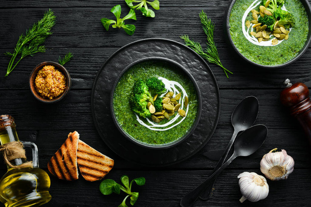 Green cream of broccoli soup and pumpkin seeds in black bowl. Top view. Free space for your text. Rustic style. - Valokuva, kuva
