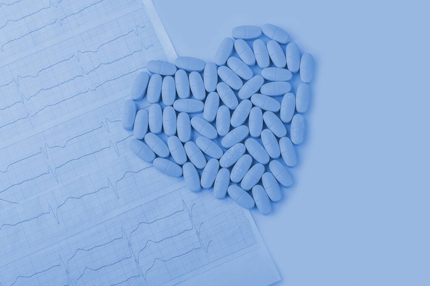 Cardiogram with red heart made from pills (tablets) on a classic blue background close up, with copy space for text. Cardiological care. Cardiology, medical and insurance concept. - Fotó, kép