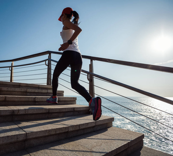 Young fitness female runner running up on seaside stairs - Photo, Image