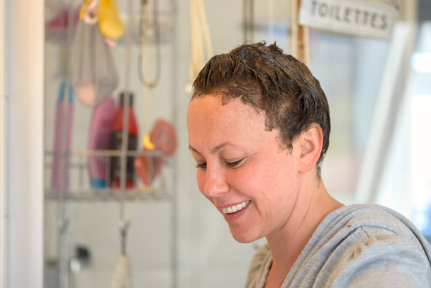 Lächelnde Frau, die ihr Haar zu Hause im Badezimmer mit Haarfärbemittel oder Farbstoff behandelt, in einem Nahaufnahme-Porträt, während sie lächelnd nach unten schaut - Foto, Bild