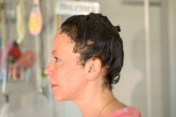 Profiel portret van een vrouw met haarverf op haar haar te wachten tot de kleur te ontwikkelen thuis in haar badkamer - Foto, afbeelding