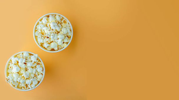 Fresh popcorn in white box on a orange background. Cinema snack concept. The food for watching a movie and entertainment. Copy space for text, top view, flat lay. - Photo, Image