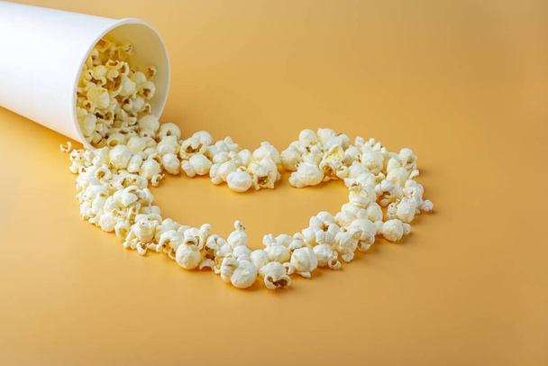 Love movies concept. Popcorn in paper box scattered on orange background heart shaped close up, copy space for text. Cinema snack concept. Popcorn box mocap - Photo, Image