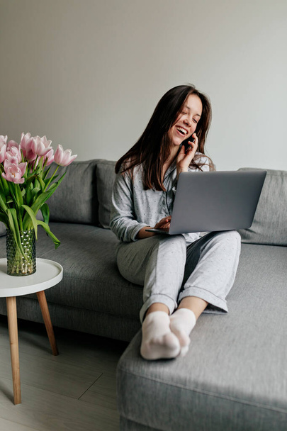 Charming pretty lady wearing home pajamas working at home with laptop and talking on the quarantine at home.  - Foto, Imagen