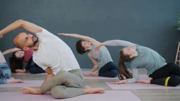Slow motion of yoga class doing Gomukhasana position then resting with hands in namaste - Felvétel, videó