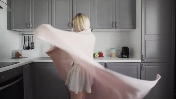 Cheerful girl spinning in a plaid and smiling in the kitchen in the morning - Materiaali, video
