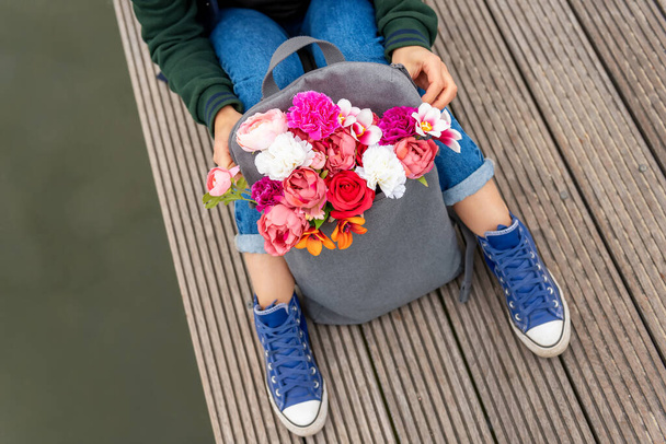 nő csokor virág szürke hátizsák mellett folyó. romantikus hangulat - Fotó, kép