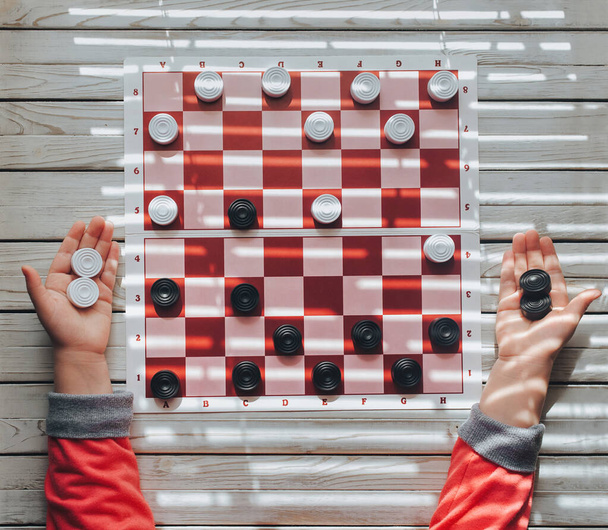 The child plays checkers. White and black checkers in children's hands. Children's school of board games. - 写真・画像