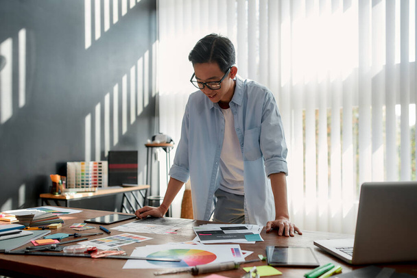 Satisfied with my work. Happy asian man in eyeglasses analyzing new design project and smiling while standing in the modern office - Fotoğraf, Görsel