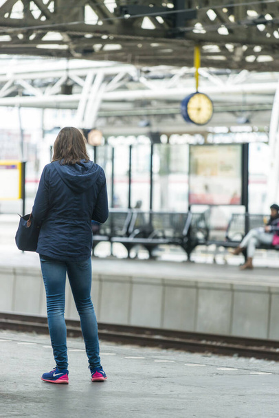 AMSTERDAM, NIDERLANDY - LIPIEC 8, 2015: Młody w dżinsach, z powrotem, czekać na peronie przyjazdu pociągu. - Zdjęcie, obraz