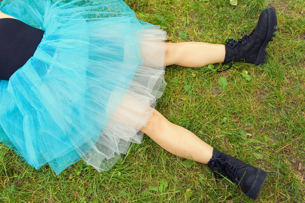 Woman in big black boots and a blue skirt lies on green grass. After party concept - Photo, Image