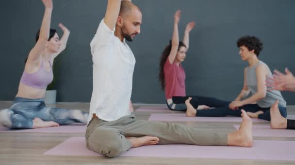 Flexible girls and guy in sportswear enjoying yoga practice in cozy room in sports center - Filmati, video