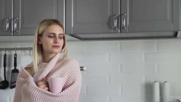 Menina bonito em um cobertor xadrez bebe chá e olha para a janela na cozinha pela manhã
 - Filmagem, Vídeo