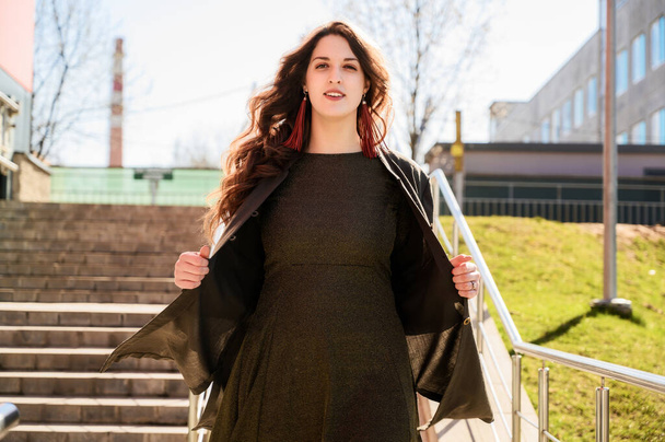 Photo of a pretty fashionable brunette woman with long beautiful hair with a smile in a suit on the background of the steps of the building in sunny weather - Valokuva, kuva