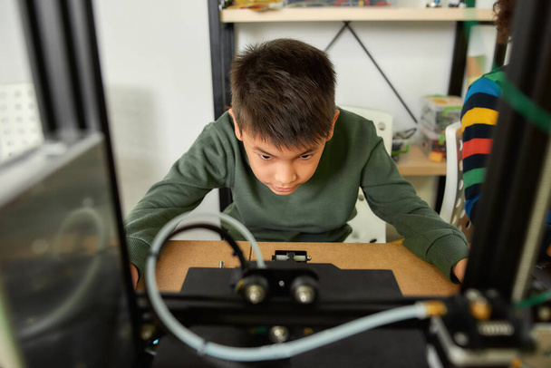 Get In the Process. Close up of curious boy learning more about working principle of 3d printer at robotics class. Progressive modern additive technology. 4th industrial revolution. - Photo, image