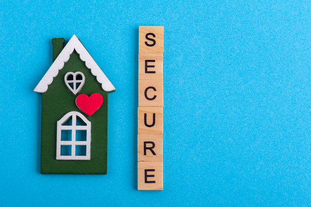 Green wooden house and Secure sign on blue background with copy space. Safety or quarantine concept, home protection, real estate insurance, private property - Photo, Image