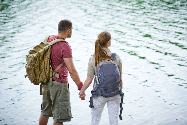 Two travelers holding hands while standing near lake at sunny day  - Photo, Image