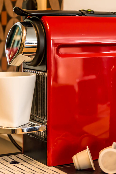 Fazer café: close-up de uma máquina de café à base de xícara vermelha, derramando café em uma caneca branca
 - Foto, Imagem