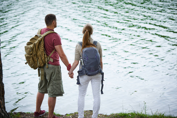 Two travelers holding hands while standing near lake at sunny day  - Photo, Image