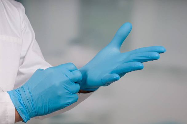Primo piano di mano indossare guanti medici di fronte a una stanza della clinica
 - Foto, immagini