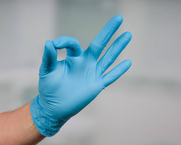 Primer plano de la mano con guantes médicos en frente de una sala de la clínica haciendo buen gesto
 - Foto, Imagen