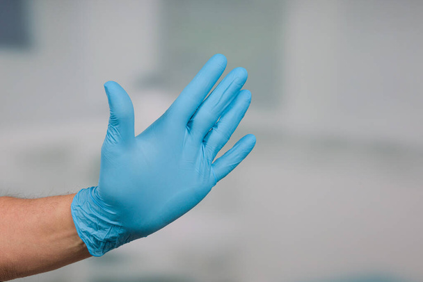 Primer plano de la mano con guantes médicos en frente de una sala de la clínica
 - Foto, Imagen