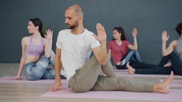 Youth male and female busy with yoga asanas sitting on mats in light studio - Filmati, video