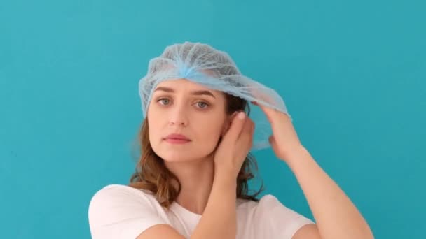 Calm young woman putting on blue medical hat - Footage, Video