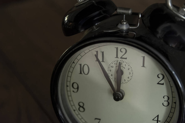 Reloj analógico vintage y retro que indica que el tiempo está casi terminado, son cinco minutos para la medianoche, fondo oscuro
.  - Foto, imagen