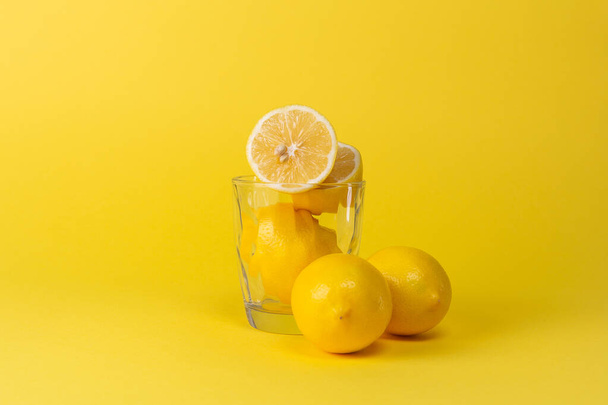 黄色の背景にレモンと空のガラスカップ - 写真・画像