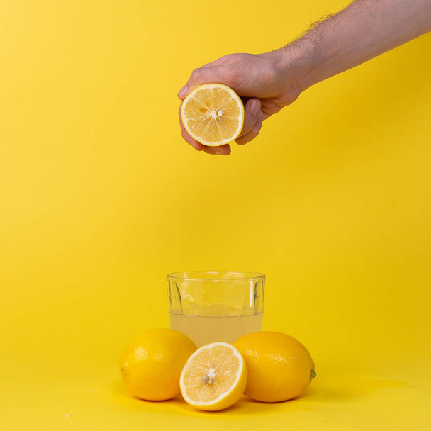 squeezing lemon juice into glass on yellow background - Fotografie, Obrázek