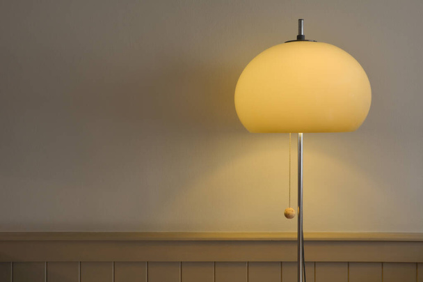 Vintage and retro 70's style floor lamp standing against a grey wall, with brown wooden paneling. Lights lit. Interior design.  - Photo, Image