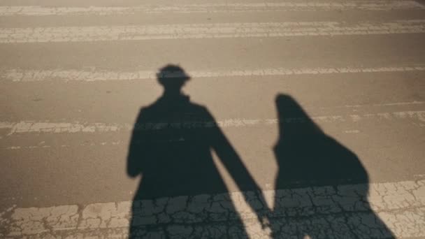 Shadow of young couple in love on pavement. Silhouette of couple holding each other hand during walk around city crossing street - Footage, Video